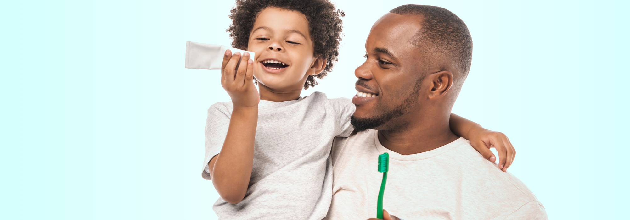 Père et son enfant souriants tenant un tube de dentifrice et une brosse à dents à poils souples